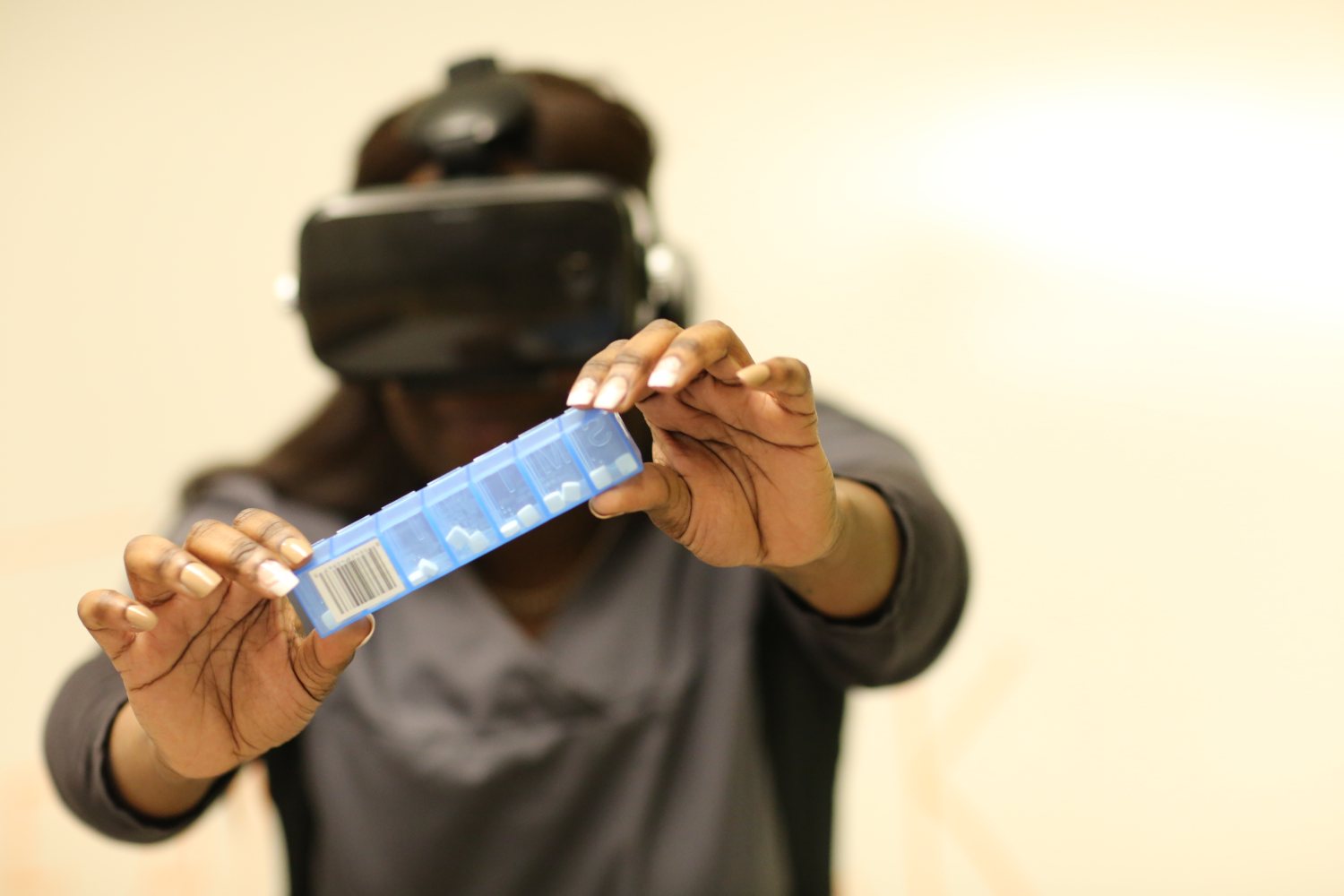 A caregiver wearing an augmented reality headset holds a weekly pill box out in front of her, trying to work out how to open it