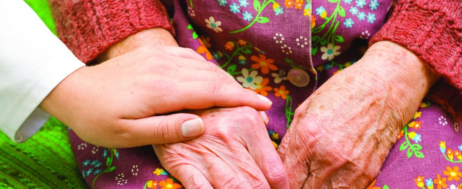 A caregiver's hand resting on a resident's hands